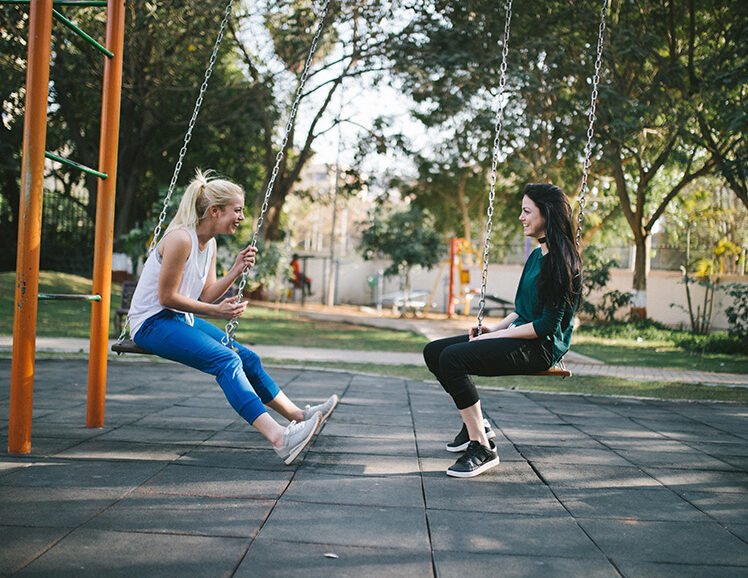 Two women sitting on swings while talking